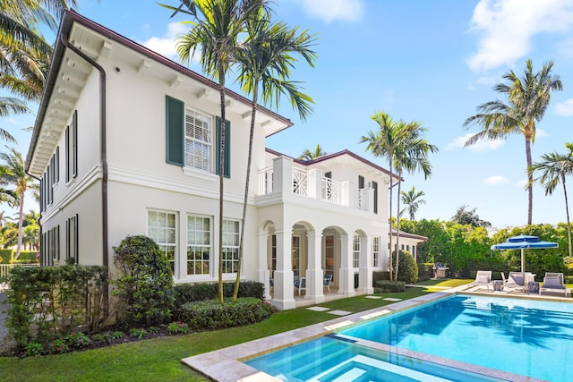 rear view of property featuring a patio area, stucco siding, a pool with connected hot tub, and a balcony