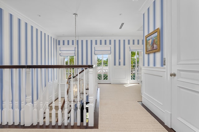 hallway with wallpapered walls, crown molding, a decorative wall, carpet flooring, and wainscoting