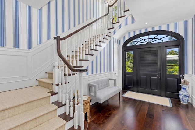 foyer with a wainscoted wall, wallpapered walls, wood finished floors, stairway, and a decorative wall