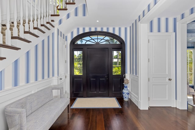 entryway featuring wallpapered walls, stairway, wood finished floors, and a wainscoted wall