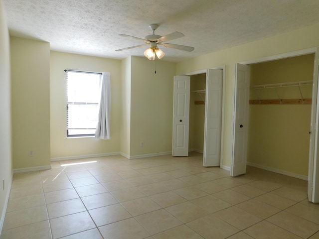 unfurnished bedroom featuring light tile patterned floors, a ceiling fan, baseboards, a textured ceiling, and two closets