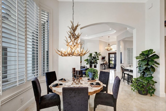 dining space with a raised ceiling, baseboards, arched walkways, and a chandelier