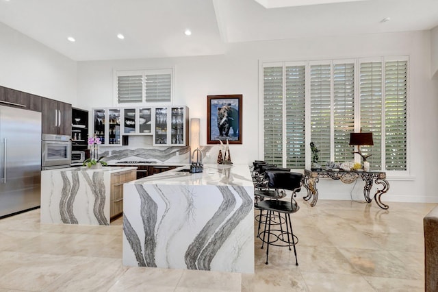 kitchen featuring light stone counters, stainless steel appliances, glass insert cabinets, a kitchen breakfast bar, and modern cabinets