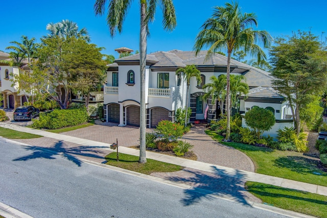 mediterranean / spanish home featuring a tiled roof, decorative driveway, a balcony, and stucco siding