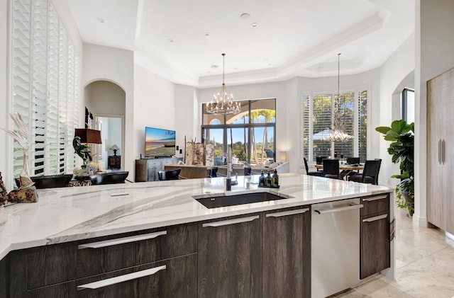 kitchen with a sink, a tray ceiling, stainless steel dishwasher, dark brown cabinetry, and an inviting chandelier