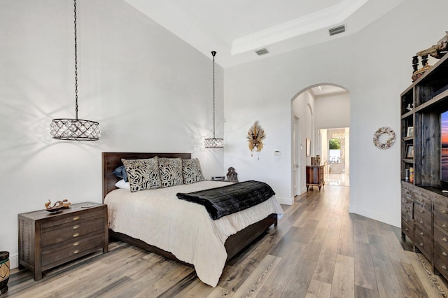 bedroom featuring wood finished floors, visible vents, arched walkways, and a tray ceiling