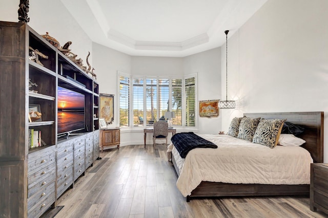 bedroom with baseboards, a raised ceiling, wood finished floors, and crown molding