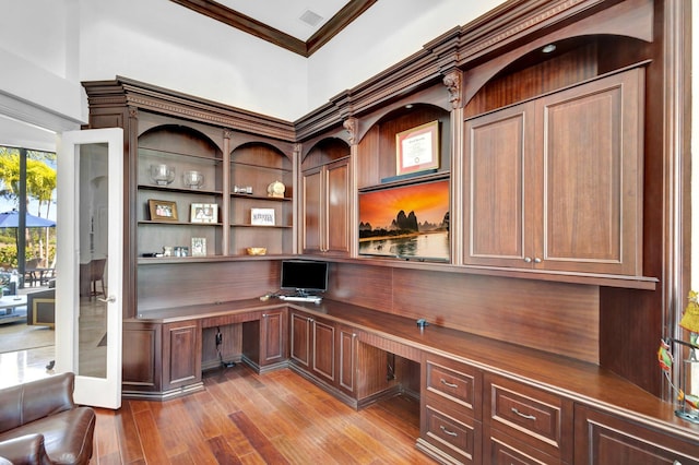 unfurnished office featuring visible vents, wood finished floors, ornamental molding, and built in study area