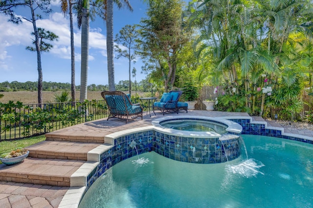 view of pool with fence and a pool with connected hot tub