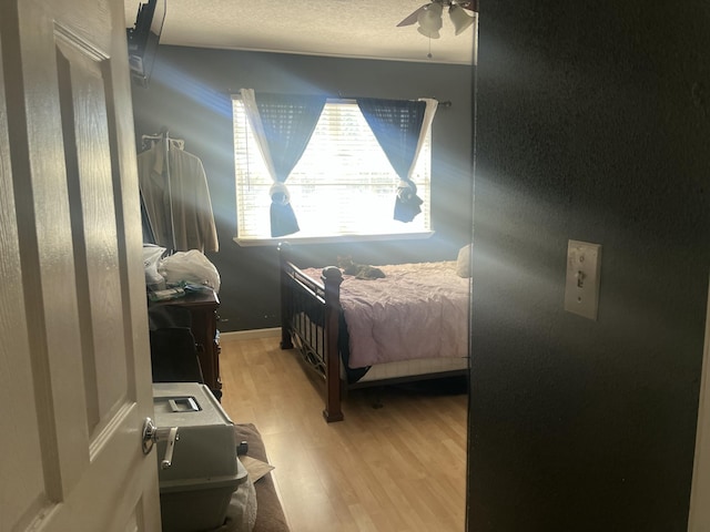 bedroom with baseboards, a textured ceiling, light wood-type flooring, and ceiling fan