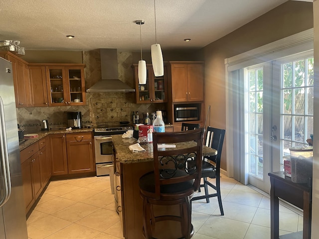 kitchen with backsplash, light tile patterned flooring, stainless steel appliances, and wall chimney exhaust hood