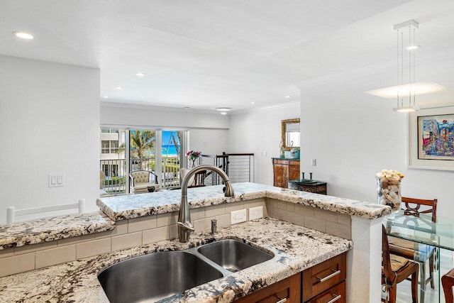 kitchen with light stone counters, recessed lighting, a sink, crown molding, and decorative light fixtures