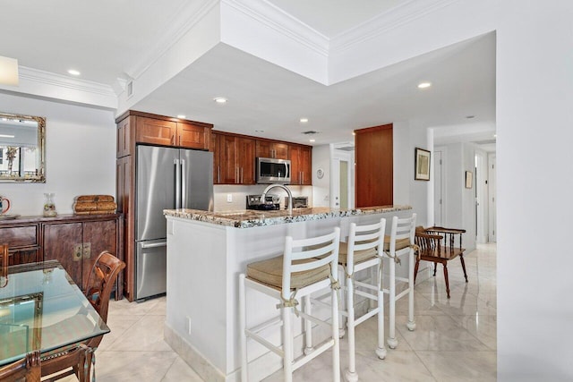 kitchen featuring a breakfast bar, crown molding, light stone counters, and appliances with stainless steel finishes