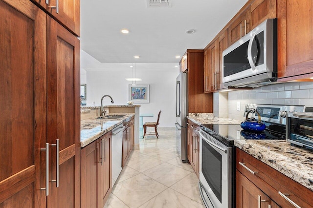 kitchen with backsplash, light stone countertops, appliances with stainless steel finishes, brown cabinetry, and a sink