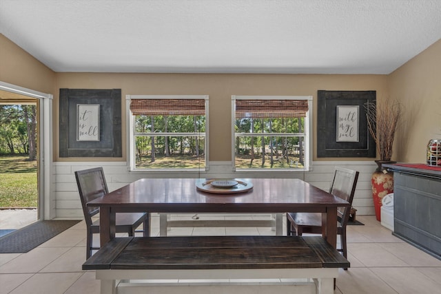 dining room with light tile patterned floors, a wainscoted wall, and a textured ceiling