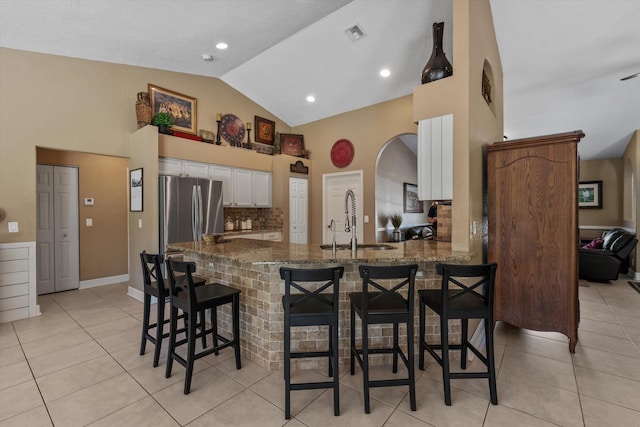 kitchen featuring a kitchen breakfast bar, freestanding refrigerator, white cabinets, stone countertops, and a sink