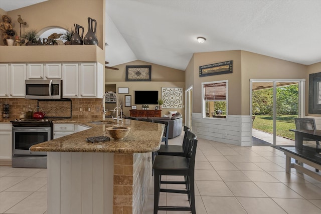 kitchen with a sink, appliances with stainless steel finishes, a peninsula, white cabinets, and lofted ceiling