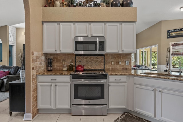 kitchen with a sink, stone countertops, appliances with stainless steel finishes, light tile patterned floors, and decorative backsplash