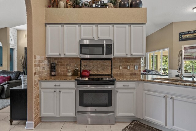 kitchen with a peninsula, white cabinetry, vaulted ceiling, appliances with stainless steel finishes, and a sink