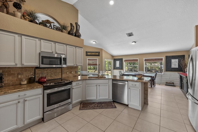 kitchen with a sink, stainless steel appliances, a peninsula, light tile patterned flooring, and vaulted ceiling