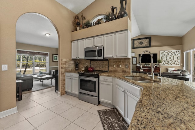 kitchen featuring light tile patterned floors, stone counters, lofted ceiling, a sink, and appliances with stainless steel finishes