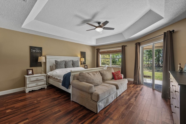 bedroom featuring a tray ceiling, baseboards, dark wood-style floors, and access to outside