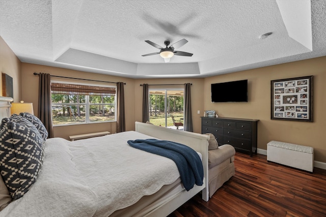 bedroom featuring a ceiling fan, wood finished floors, baseboards, a textured ceiling, and a raised ceiling