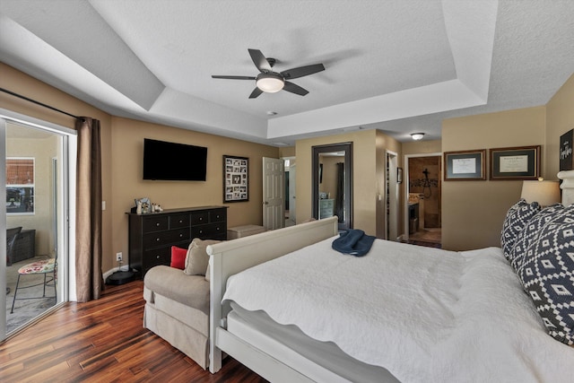 bedroom with a tray ceiling, dark wood-type flooring, and a textured ceiling