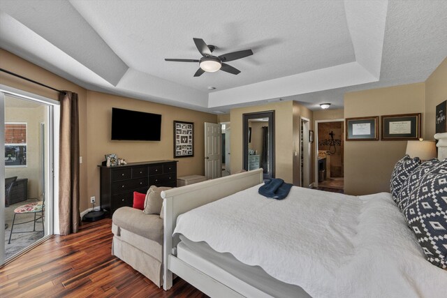 bedroom featuring baseboards, a textured ceiling, a tray ceiling, ceiling fan, and wood finished floors
