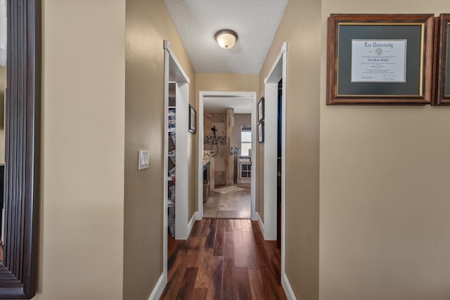 hallway with dark wood-style floors, a textured ceiling, and baseboards