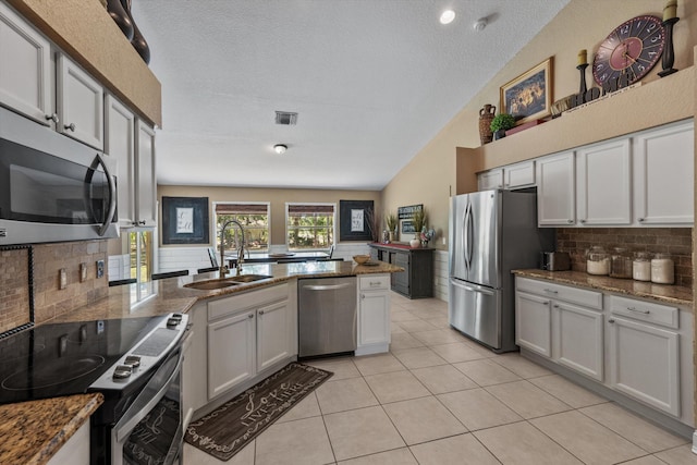 kitchen featuring visible vents, a peninsula, lofted ceiling, a sink, and stainless steel appliances