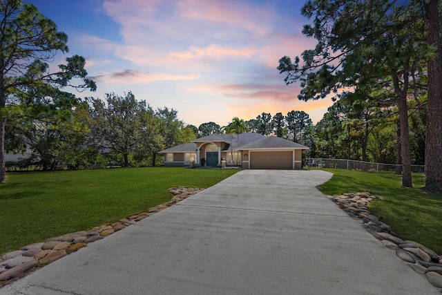 view of front facade with a yard, driveway, a garage, and fence