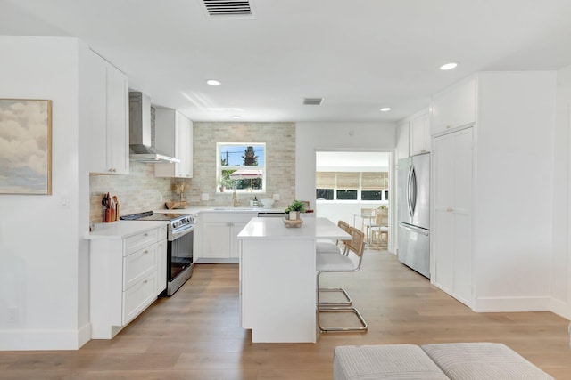 kitchen with light wood finished floors, appliances with stainless steel finishes, wall chimney exhaust hood, and light countertops