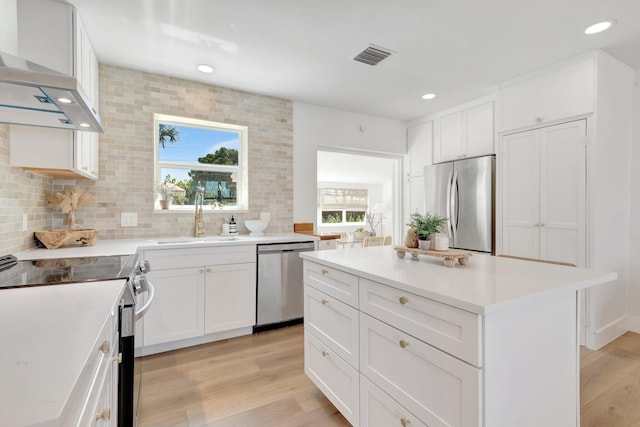 kitchen featuring backsplash, wall chimney range hood, light wood-type flooring, appliances with stainless steel finishes, and a sink