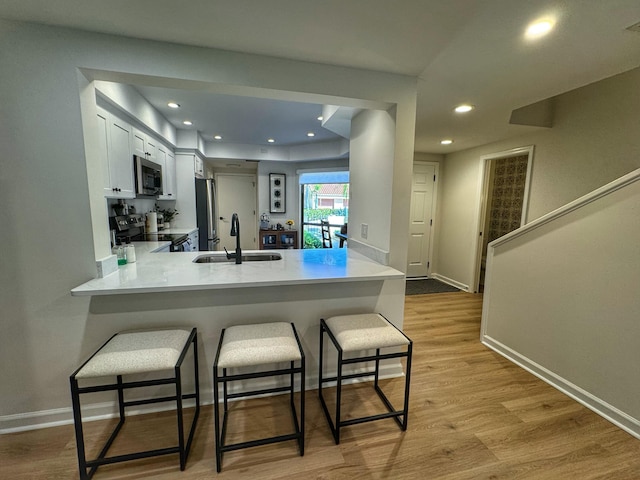 kitchen featuring a breakfast bar, a sink, light wood-style floors, appliances with stainless steel finishes, and a peninsula