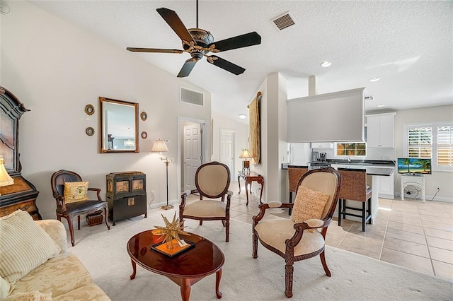 living area featuring vaulted ceiling, light tile patterned flooring, visible vents, and ceiling fan