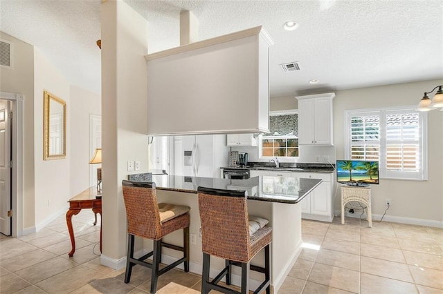 kitchen featuring visible vents, a breakfast bar, light tile patterned floors, white refrigerator with ice dispenser, and white cabinets