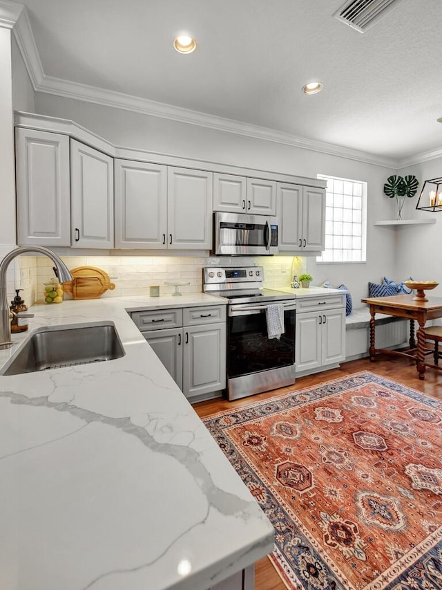 kitchen with backsplash, crown molding, light wood-style floors, stainless steel appliances, and a sink