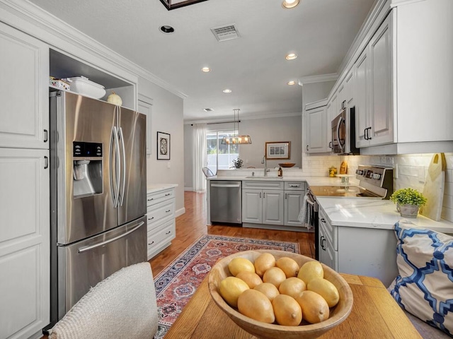 kitchen featuring backsplash, ornamental molding, wood finished floors, stainless steel appliances, and a sink