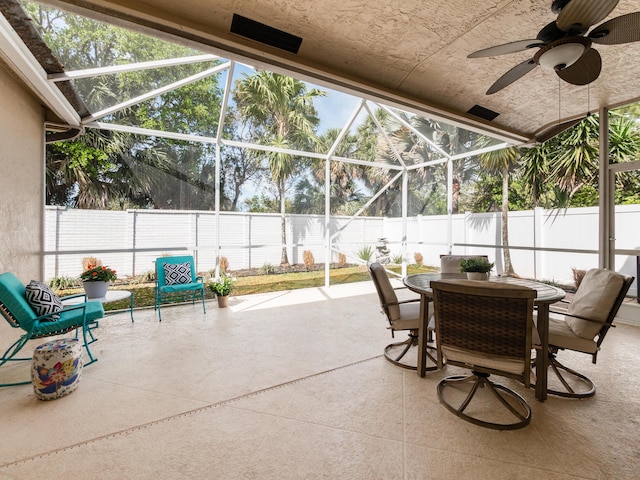 view of patio / terrace featuring glass enclosure, outdoor dining area, a fenced backyard, and ceiling fan