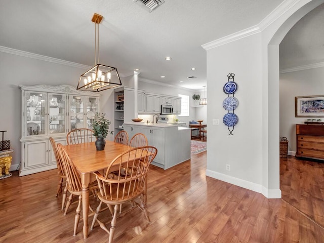 dining room featuring light wood-style floors, crown molding, arched walkways, and visible vents