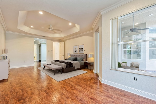 bedroom featuring a tray ceiling, wood finished floors, baseboards, and ornamental molding