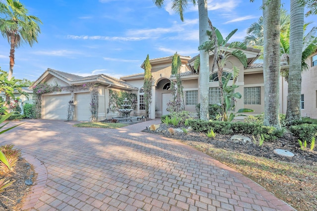 mediterranean / spanish-style house featuring stucco siding, decorative driveway, an attached garage, and a tile roof