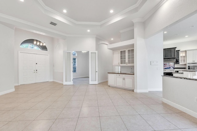 foyer entrance with visible vents, a tray ceiling, ornamental molding, light tile patterned floors, and an inviting chandelier