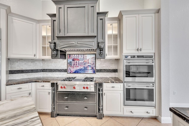 kitchen featuring decorative backsplash, light tile patterned flooring, glass insert cabinets, and appliances with stainless steel finishes