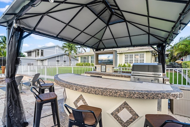 view of patio with fence, a gazebo, outdoor wet bar, a grill, and an outdoor kitchen