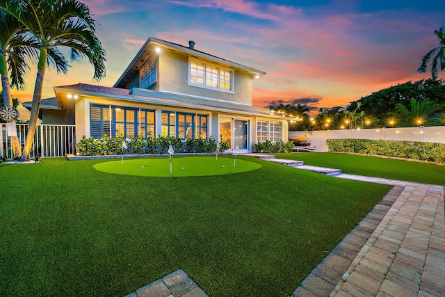 back of house at dusk with stucco siding, a lawn, and a fenced backyard