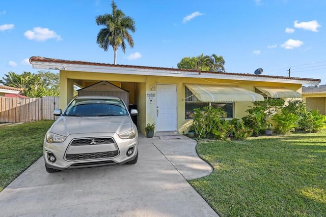 view of front facade featuring a carport, stucco siding, a front yard, and fence