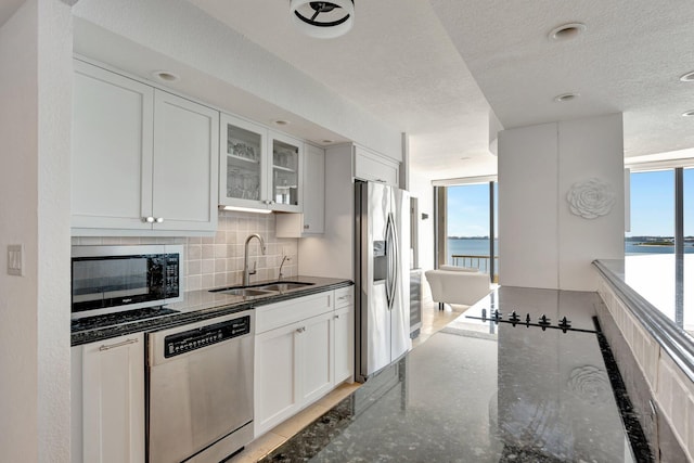 kitchen featuring tasteful backsplash, glass insert cabinets, a water view, appliances with stainless steel finishes, and a sink