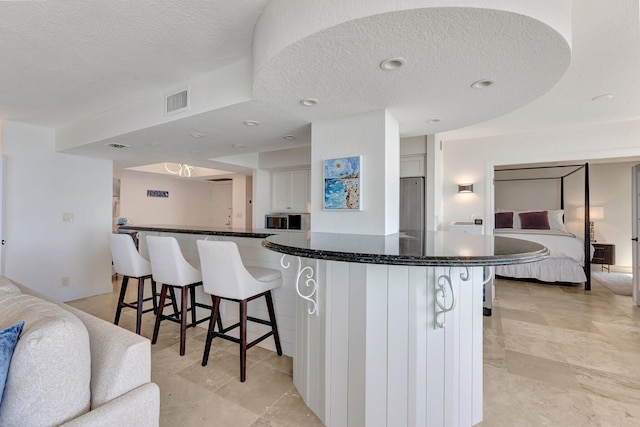 kitchen with visible vents, dark stone countertops, a kitchen breakfast bar, a textured ceiling, and white cabinetry